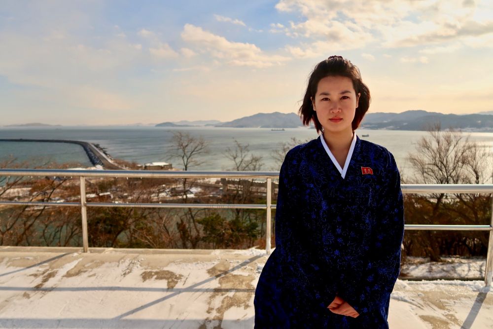A young North Korean woman in a traditional Hanbok dress poses in front of the Nampo West Sea Barrage. 