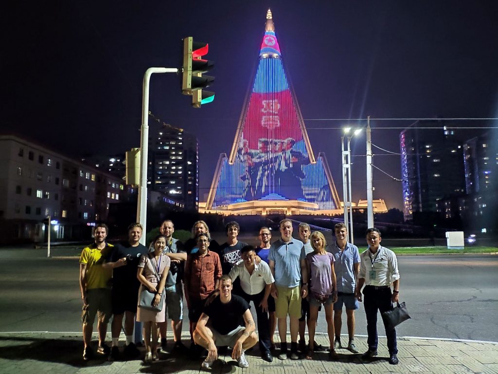 The illuminated pyramid hotel of Pyongyang stands behind our group. The illuminated Ryugyong hotel