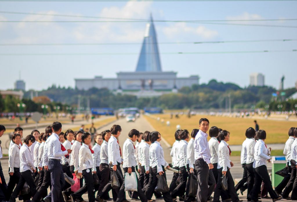 A group of North Korean students walk by the Mansudae statues where the Ryugyong hotel can be seen in North Korea