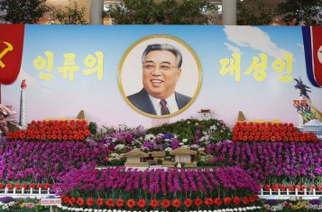 A large picture of Kim Il Sung surrounded by kimilsungia and kimjongilia flowers.