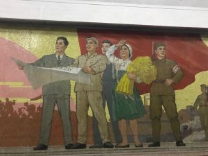 A group of factory workers and a woman carrying a bushel of wheat on a Pyongyang Metro Mural.