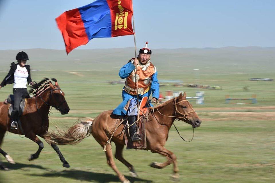 A Mongolian horseman rides past with the flag of Mongolia in the run-up to a Mongol horse race. 