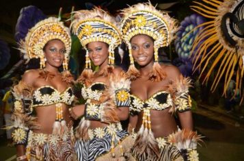 Three women in flamboyant costumes pose at the Angola Carnival.