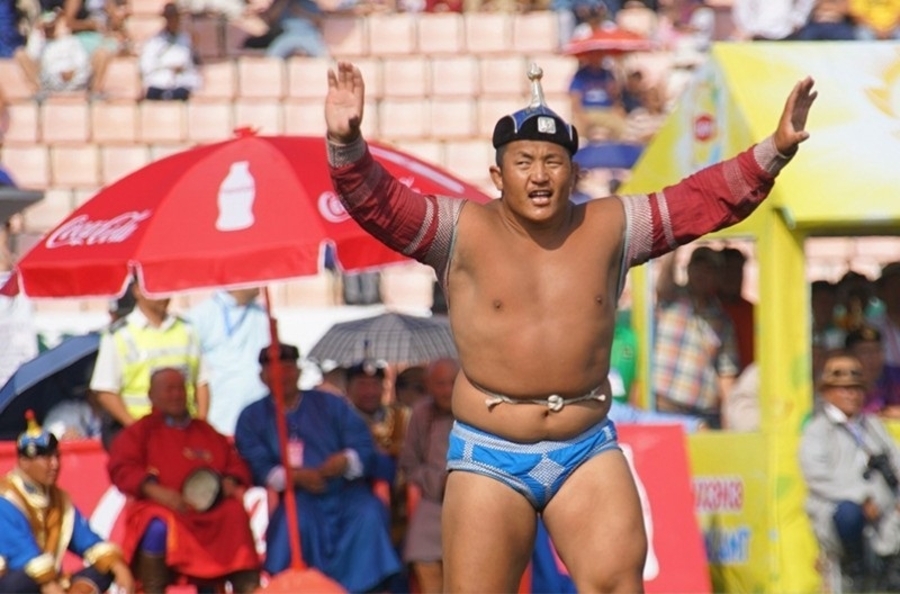A stocky Mongolian wrestler in traditional wrestling trunks prepares to fight. 