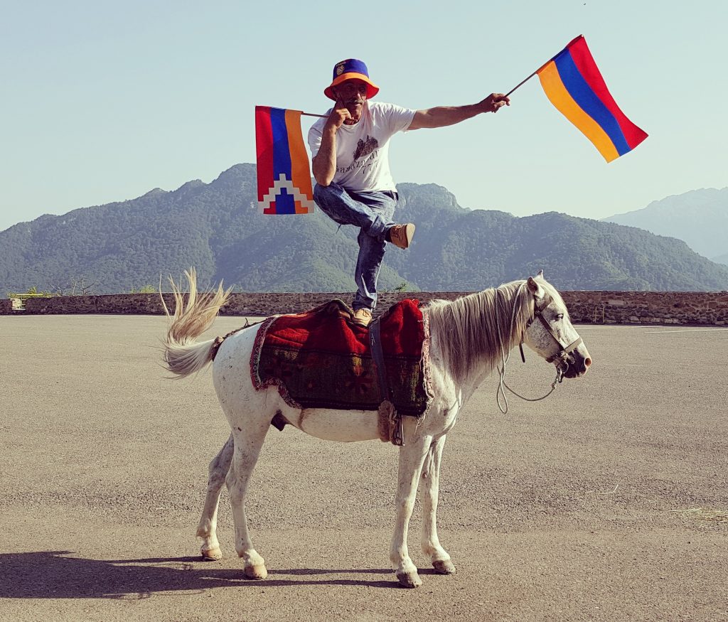 A man balances on a horse with two flags in Nagorno-Karabakh. 