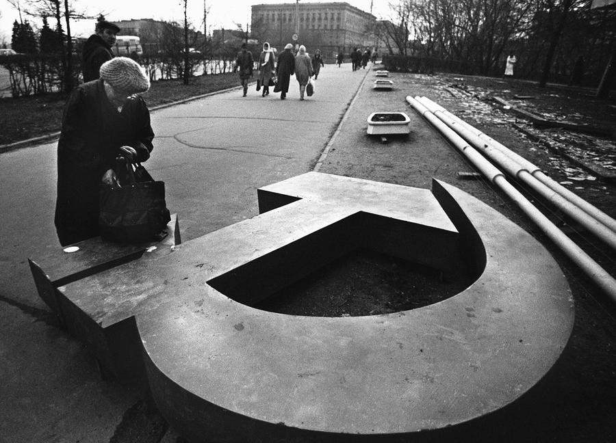 A woman looks at a downed hammer and sickle in a post-USSR country. 