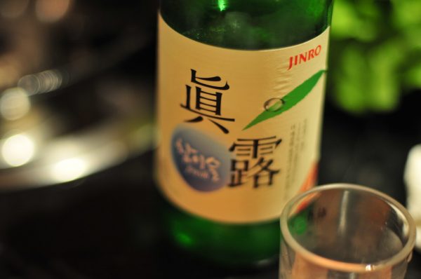 A glass of soju is being prepared next to a soju bottle